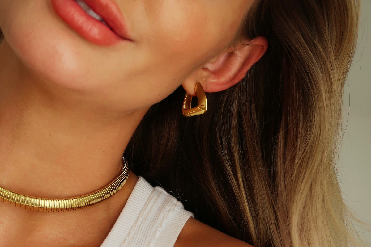 Closeup of a woman wearing a gold hoop earing and gold banded necklace