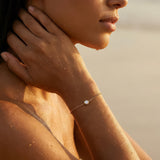 Close-up of a person wearing a delicate gold bracelet with a clear gemstone on a sunlit background