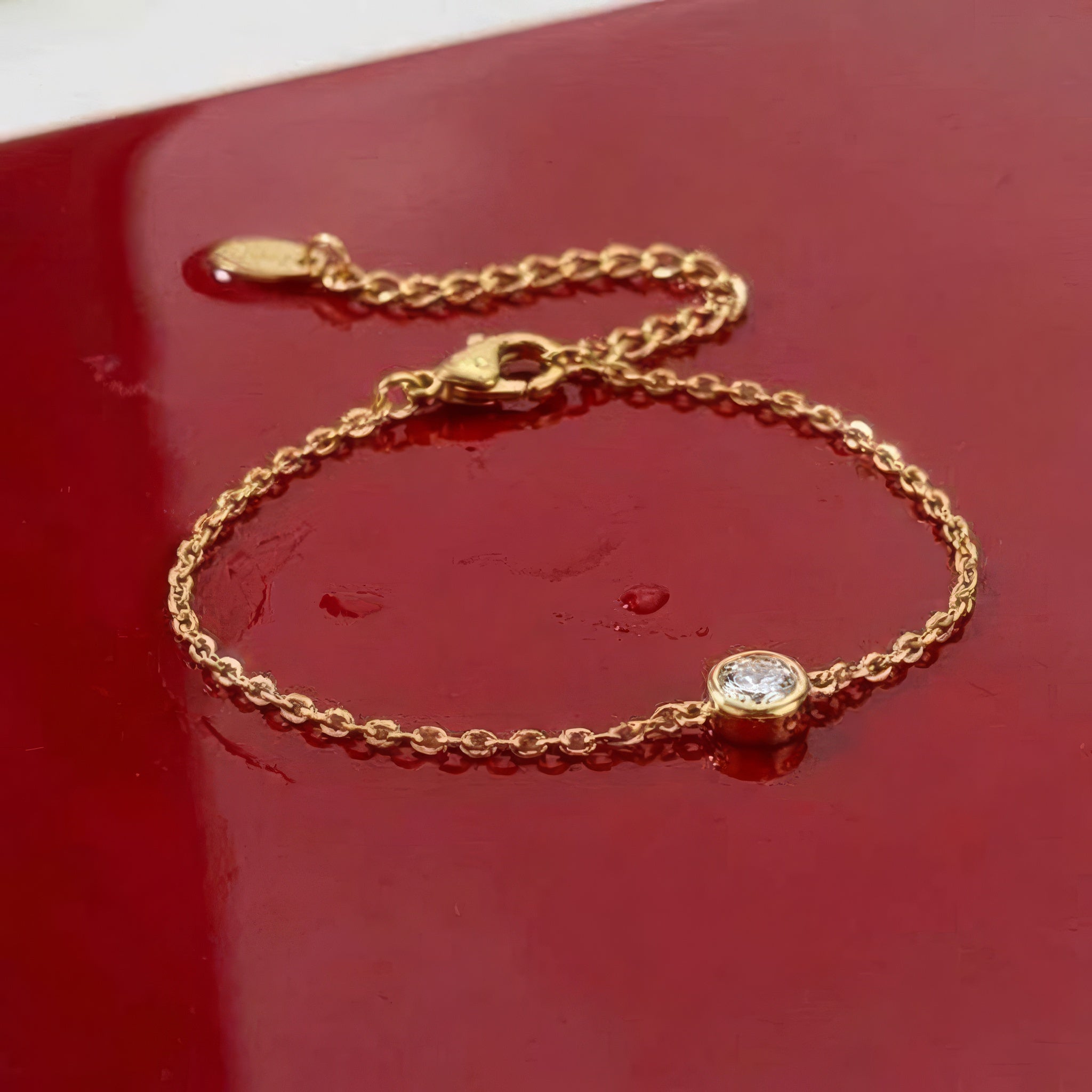 Gold bracelet with a clear gemstone on a wet red surface