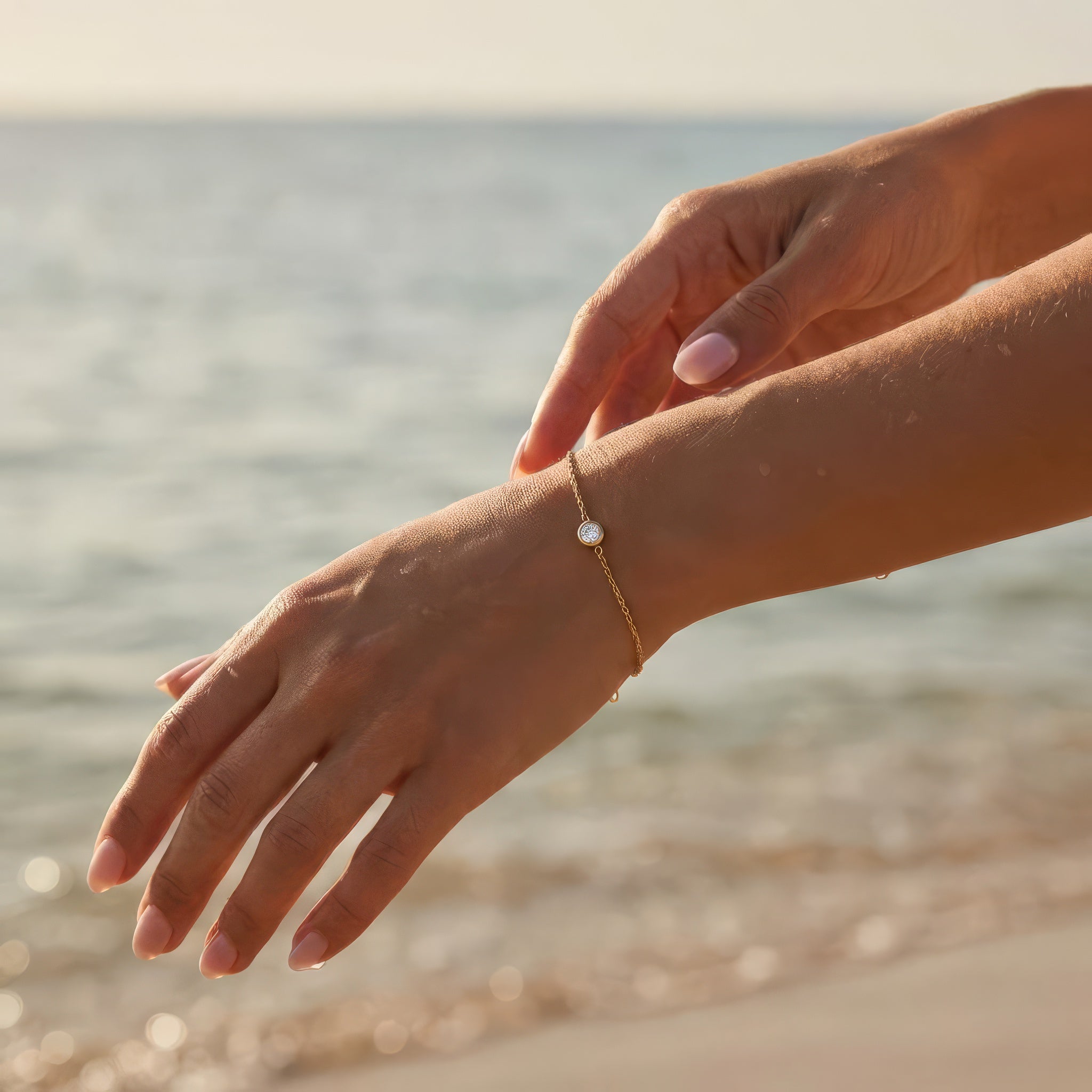 Hand wearing a gold bracelet with a clear gemstone on a beach background