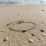 Gold bracelet with a small clear gemstone on a sandy beach