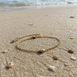 Gold bracelet with a small clear gemstone on a sandy beach