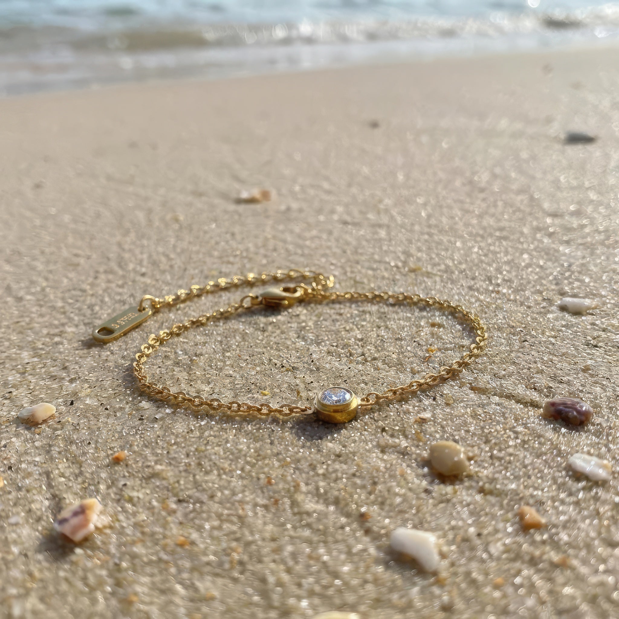 Gold bracelet with a small clear gemstone on a sandy beach