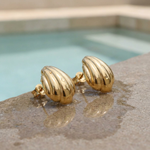 Gold shell-shaped earrings on a textured surface on the edge of a pool