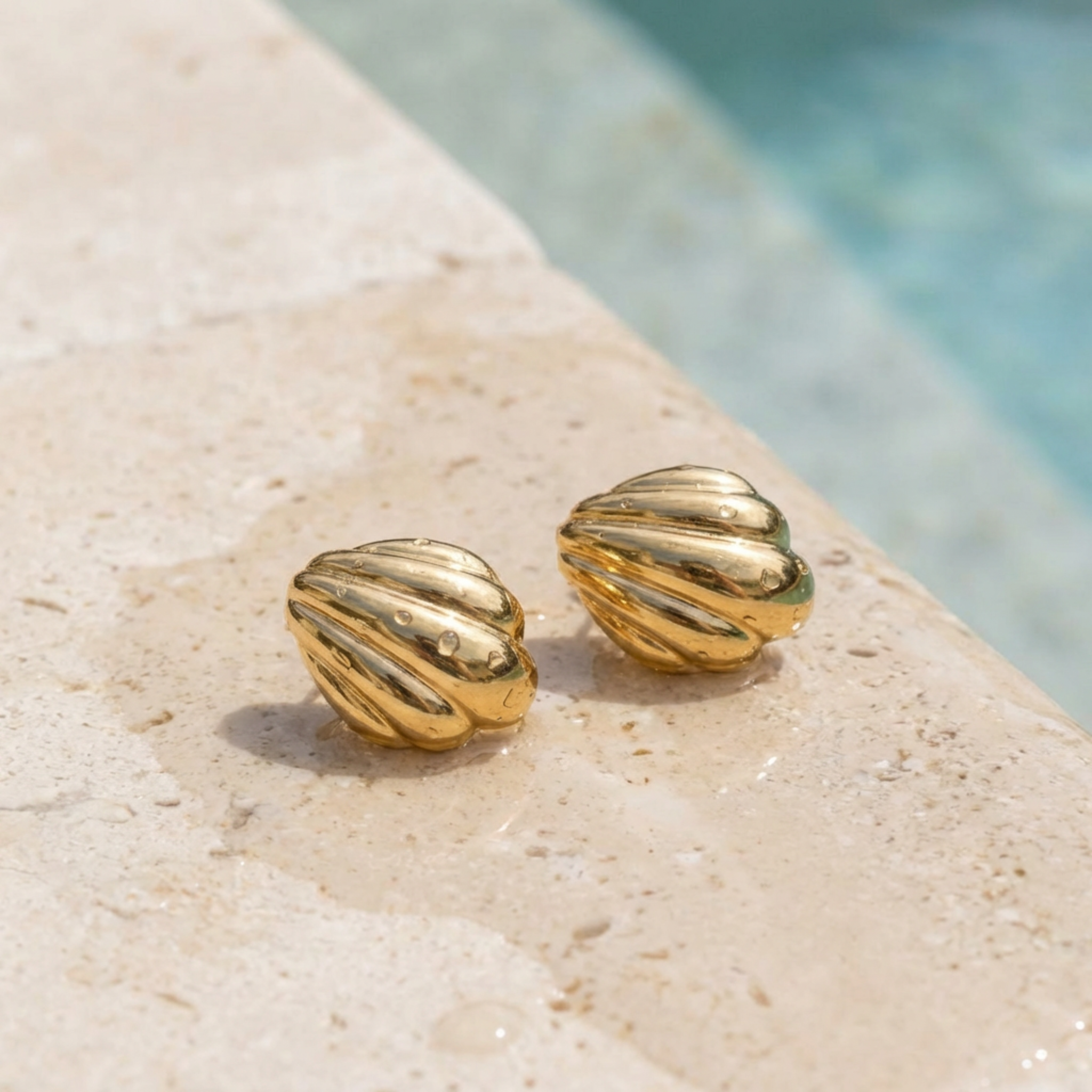 Gold shell-shaped earrings on a stone surface of a pool