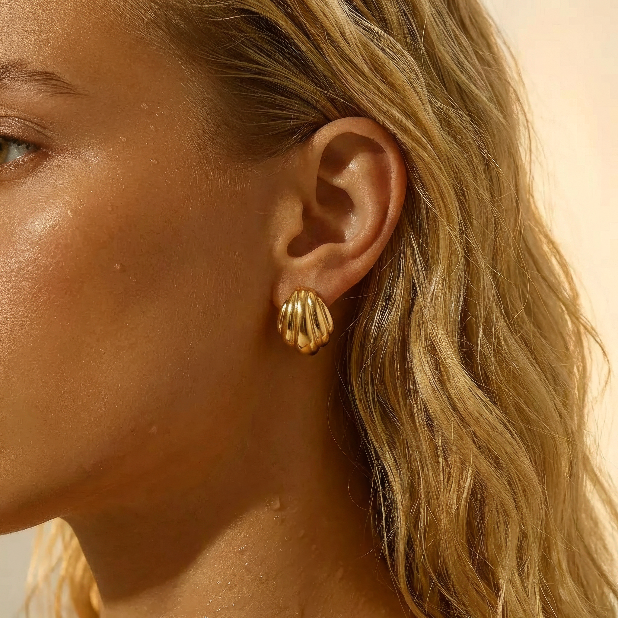 Close-up of a woman wearing gold shell-shaped earrings with a neutral background