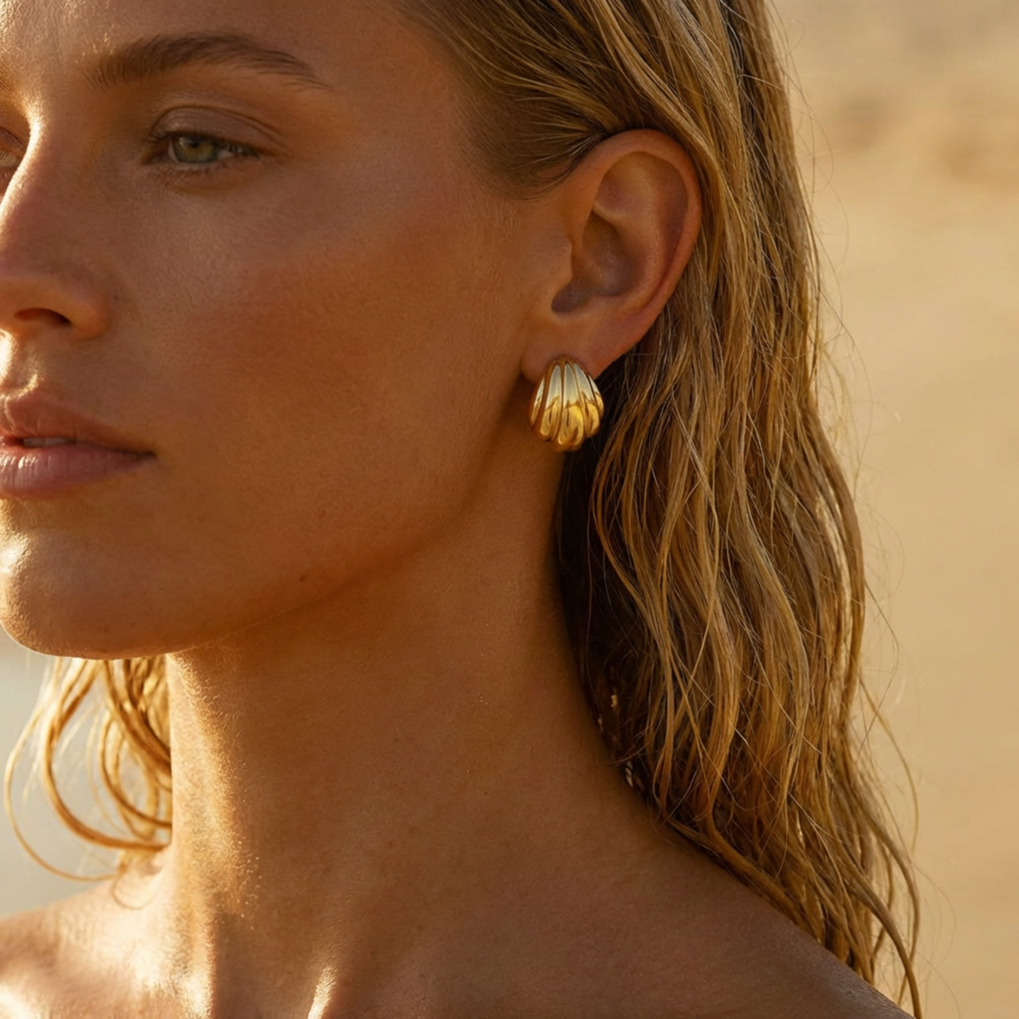 Close-up of a woman wearing gold shell-shaped earrings with a blurred background