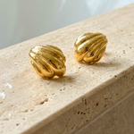 Gold earrings on a beige stone surface in a bathroom