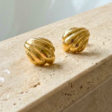 Gold earrings on a beige stone surface in a bathroom