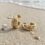 Gold hoop earrings in wet sand at the beach