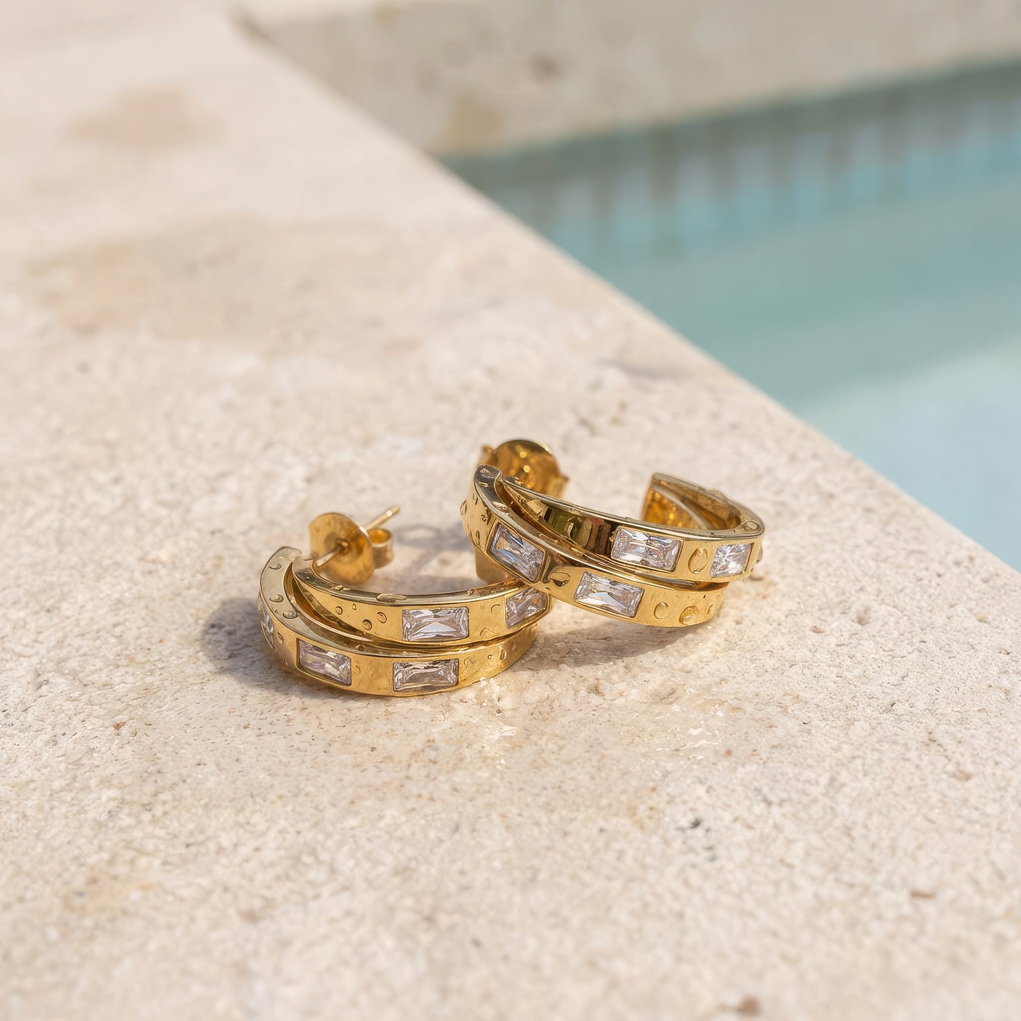 Gold hoop earrings on a wet surface at the edge of the pool