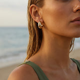 Close up of gold hoop earrings on a woman at the beach