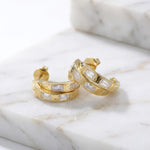 Gold hoop earrings on a wet marble surface