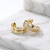 Gold hoop earrings on a wet marble surface