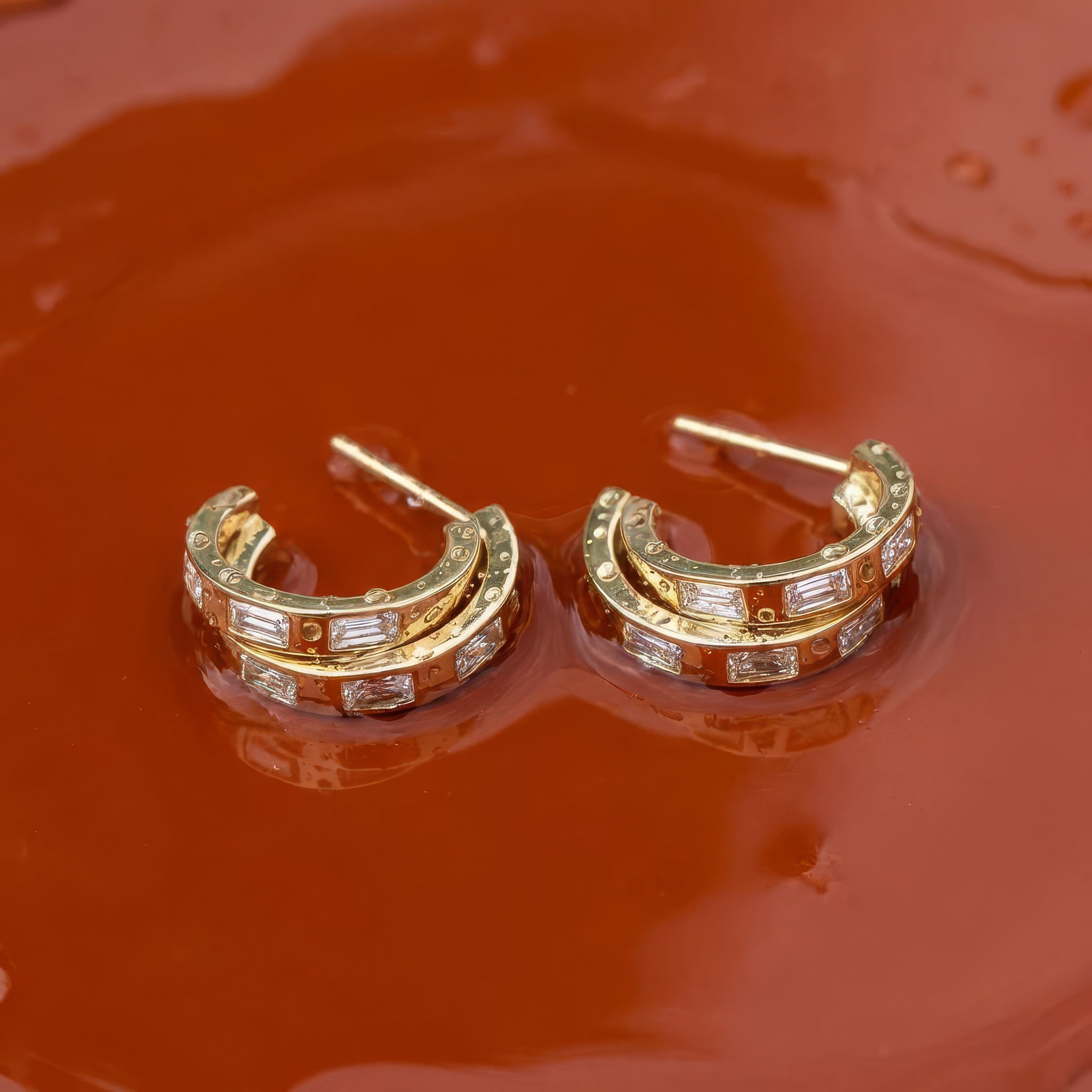 Gold hoop earrings on a wet orange surface