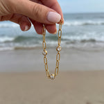 Gold chain bracelet with three diamond-like stones held in hand and dangling in the wind in front of the ocean