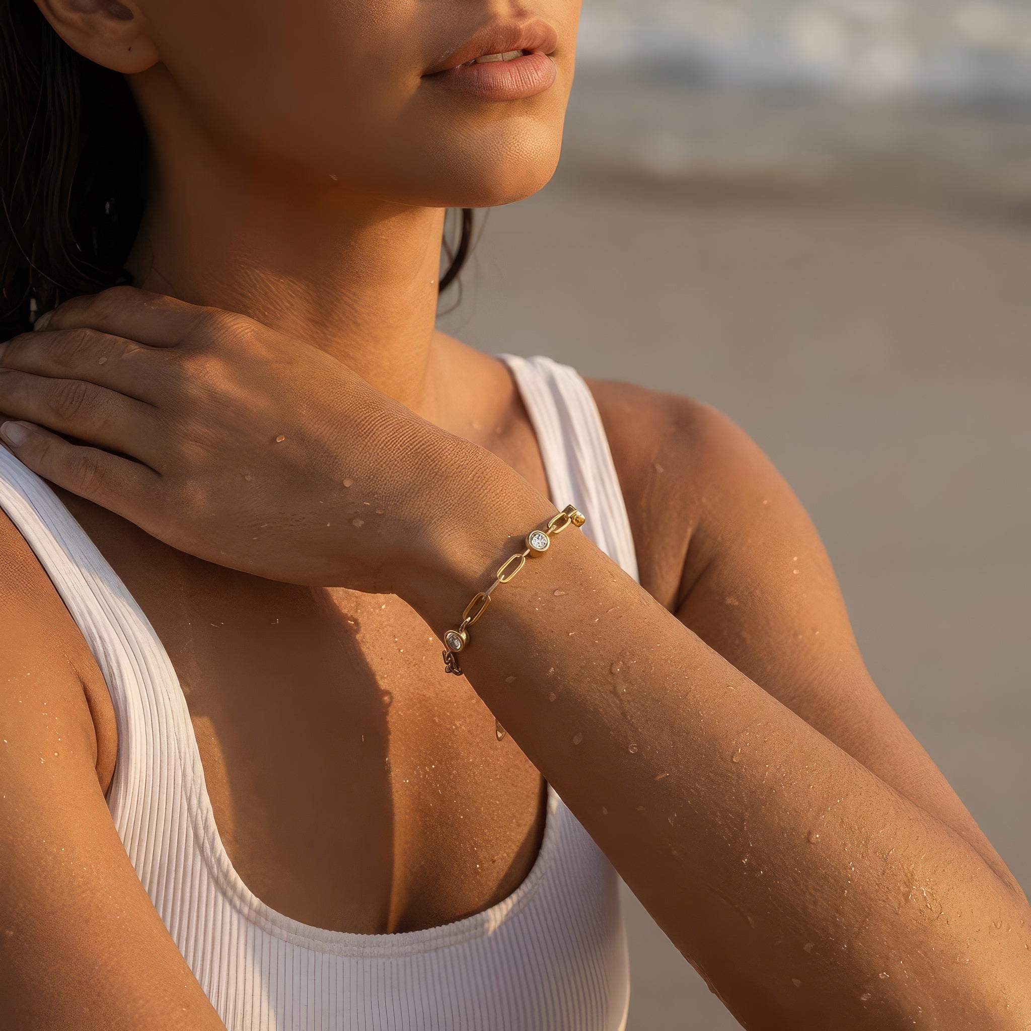 A woman at the beach wearing a gold chain bracelet with three diamond-like stones 