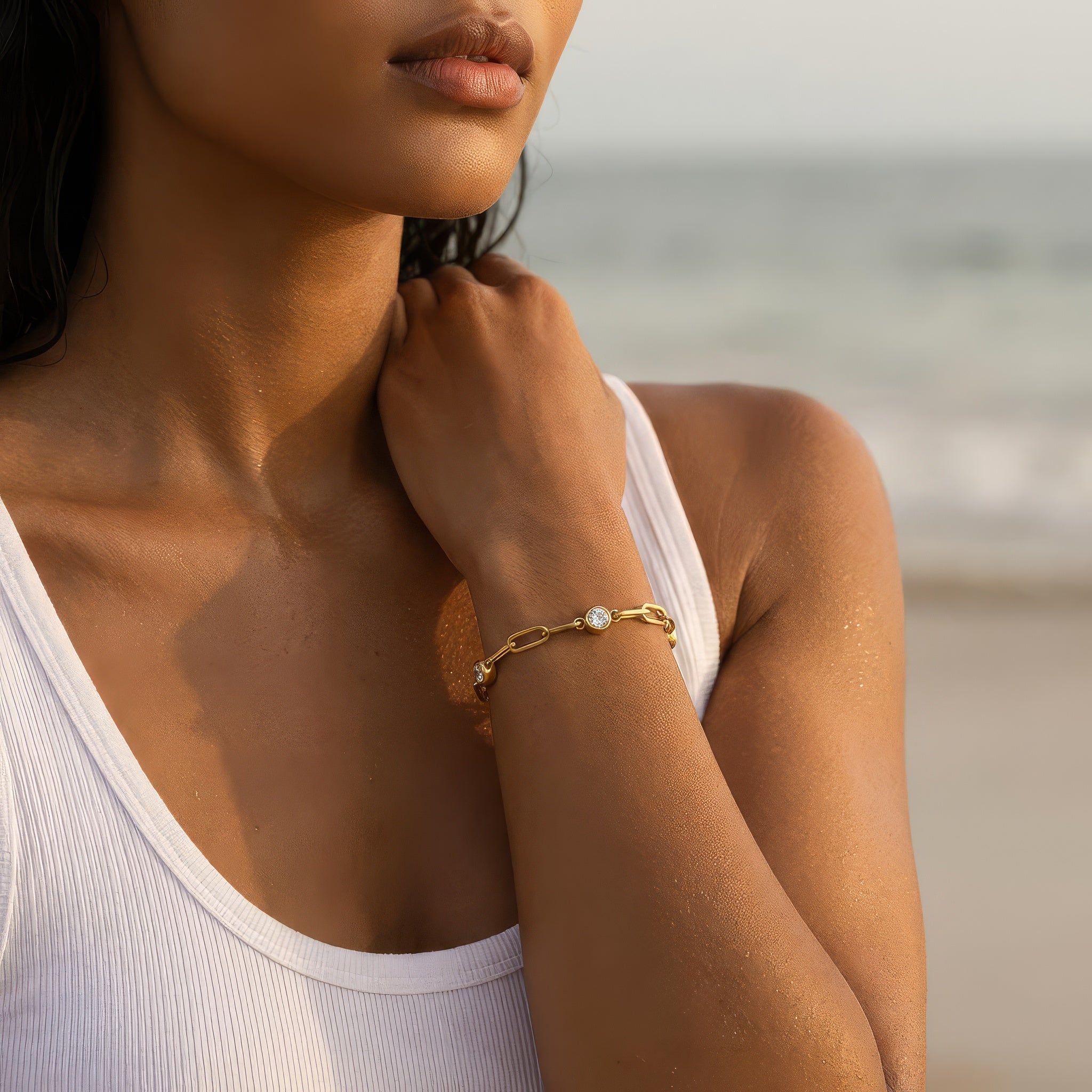 A woman at the beach wearing a gold chain bracelet with three diamond-like stones 