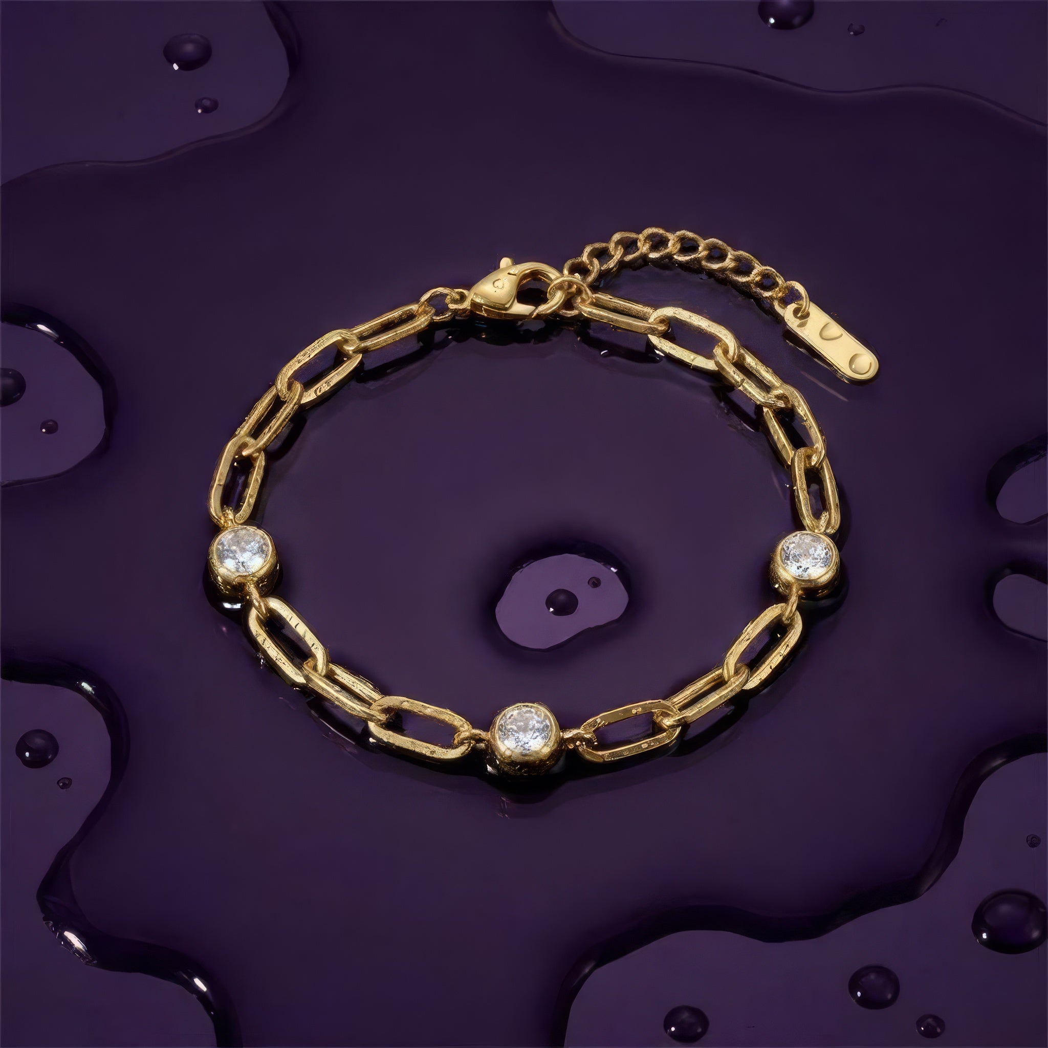Gold chain bracelet with three diamond-like stones on a wet dark purple surface