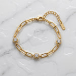 Gold chain bracelet with three diamond-like stones on a wet white marble surface