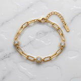 Gold chain bracelet with three diamond-like stones on a wet white marble surface