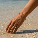 Gold chain bracelet with three diamond-like stones on a woman's wrist in front of the ocean at the beach