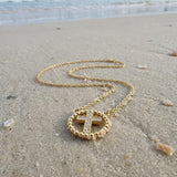 Gold cross necklace with rhinestones lying on the sand at the beach with the ocean in the background
