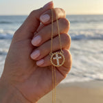 Gold cross necklace with rhinestones held in hand in front of the ocean
