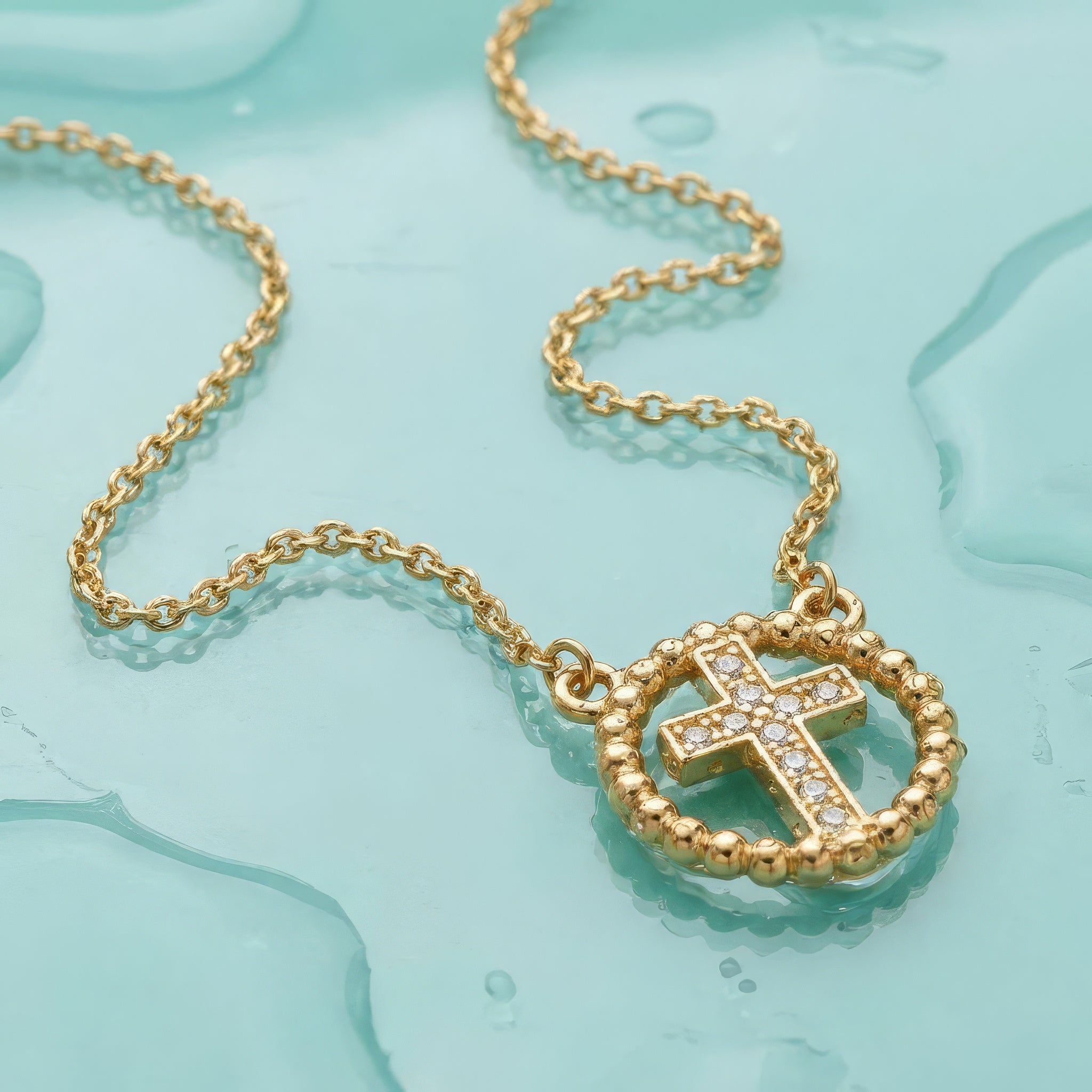 Gold cross necklace with rhinestones on a wet turquoise surface