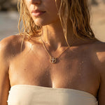 A woman wearing a gold cross necklace with rhinestones at the beach