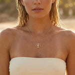A woman wearing a gold cross necklace with rhinestones at the beach