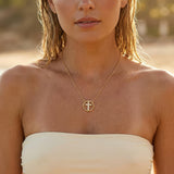 A woman wearing a gold cross necklace with rhinestones at the beach