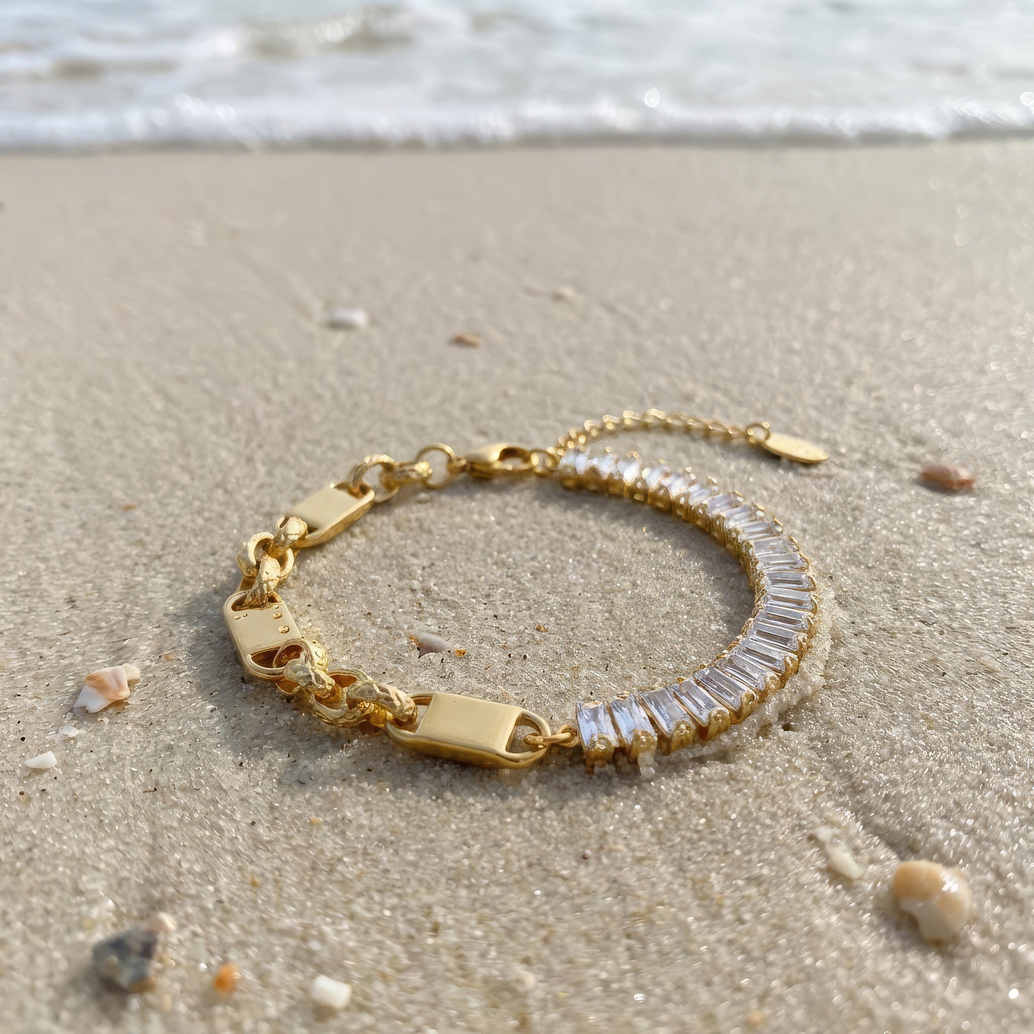 Gold bracelet with clear baguette gemstones on a sandy beach