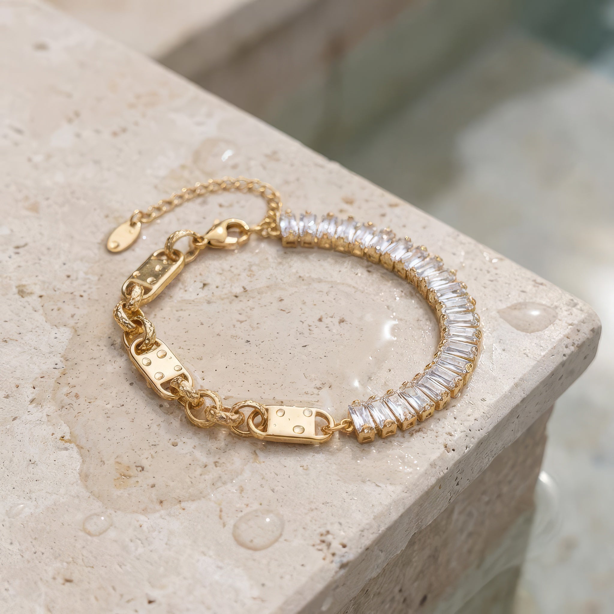 Gold bracelet with clear baguette gemstones on a textured stone surface