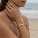 Woman on a beach wearing a gold bracelet with clear baguette crystals with a blurred background