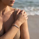 Woman on a beach wearing a gold bracelet with clear baguette gemstones with a blurred beach background