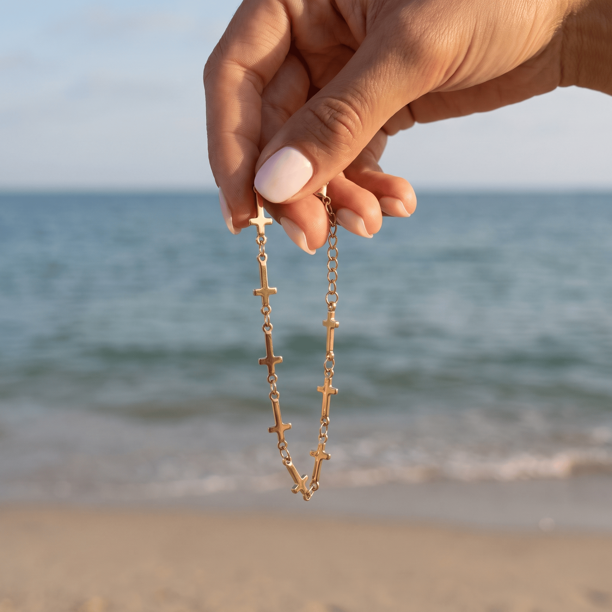 Mini Crosses Bracelet held in a hand and dangling in front of the ocean.