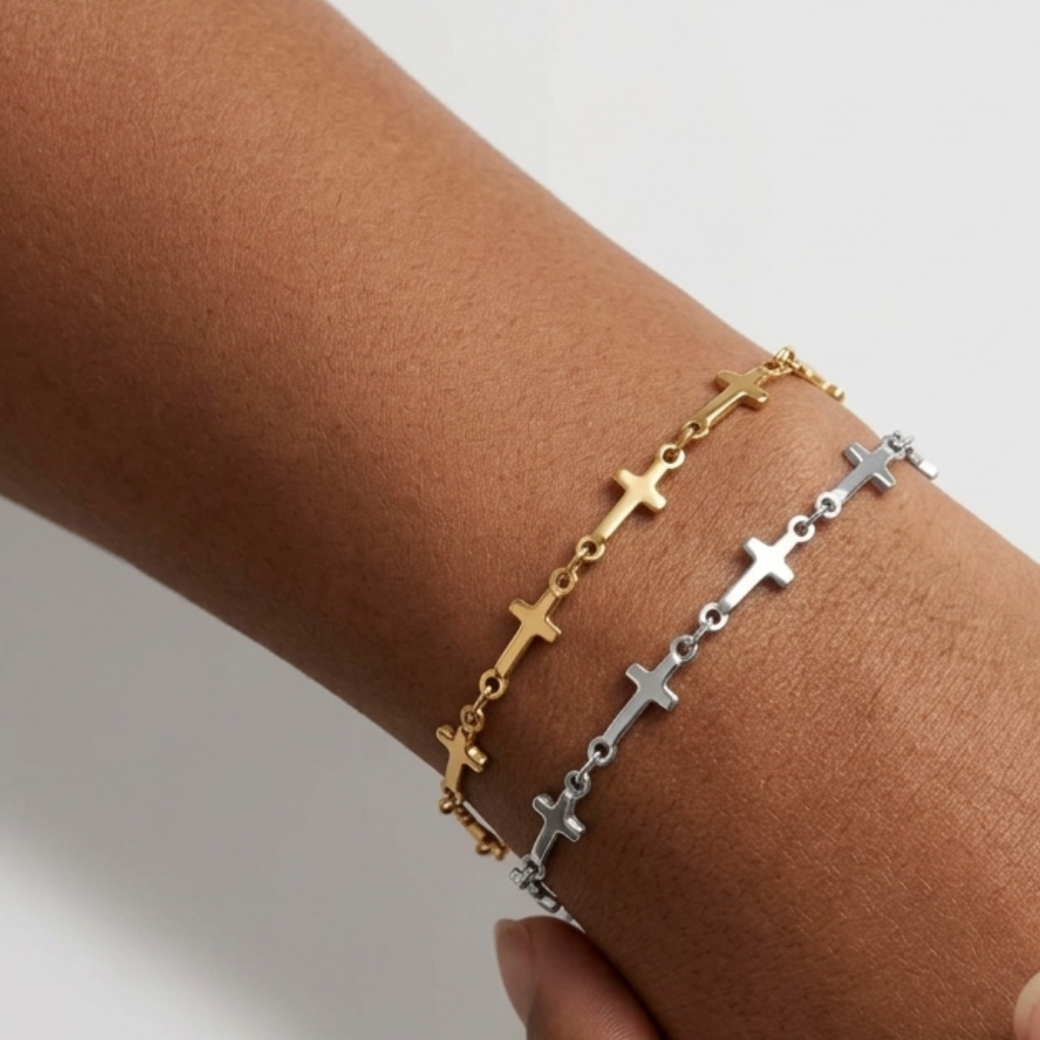 Two Mini Crosses Bracelet on a wrist with a white background. One is silver, one is gold.