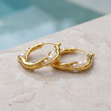 Gold hoop earrings with pearls on a stone surface at the edge of a pool.