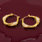 Gold hoop earrings with pearls on a wet dark red background