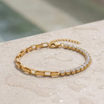 Gold bracelet with clear gemstones on a light stone surface at the edge of a pool