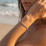 Woman on a beach with sun-kissed skin wearing a gold bracelet with clear gemstones.