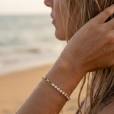 Close-up of a woman's arm with a gold bracelet with clear gemstones on a beach