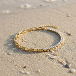 Gold bracelet with clear gemstones on a sandy surface