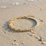 Gold bracelet with clear gemstones on a sandy surface