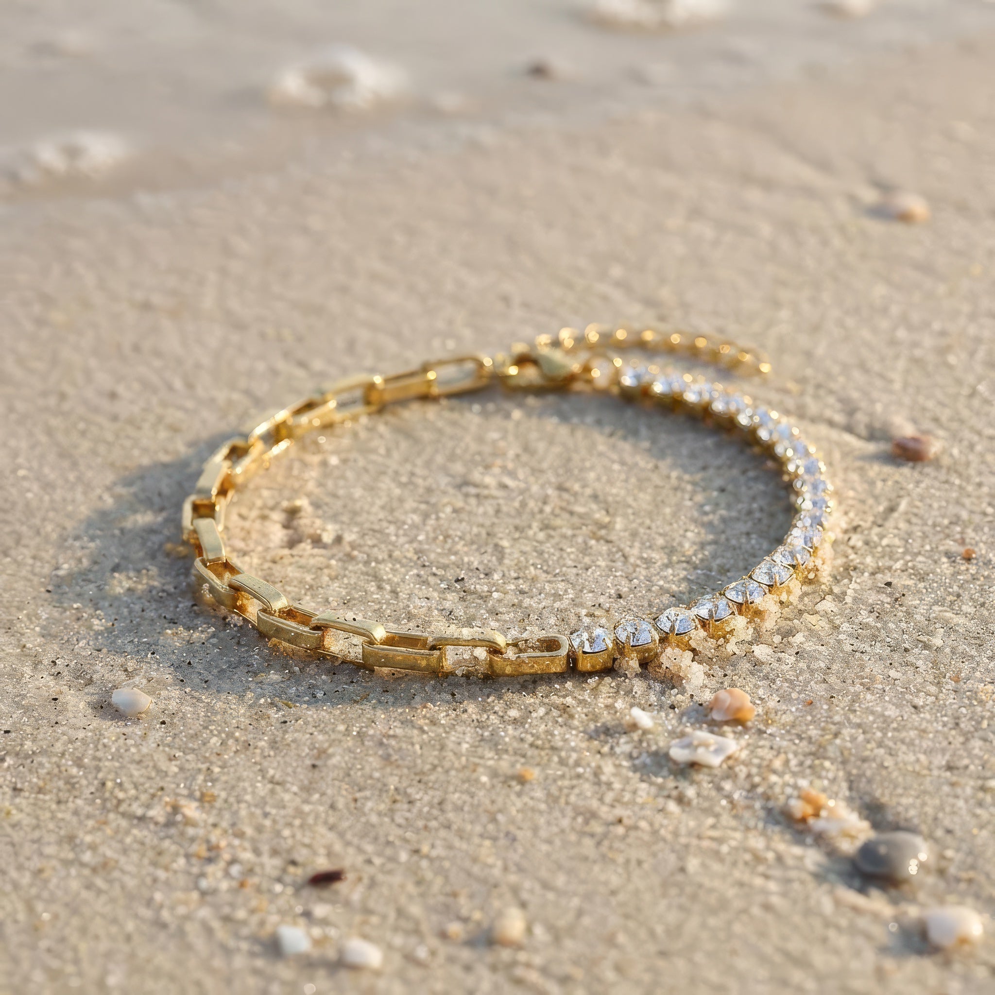 Gold bracelet with clear gemstones on a sandy surface