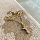 Gold cross necklace on a textured stone surface on the edge of a pool