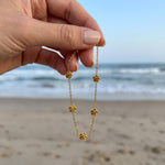 Hand holding a gold bracelet in front of the ocean with five stationary gold rosebud designs spaced out on the chain 