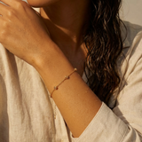 A woman wearing a gold bracelet with five stationary gold rosebud designs spaced out on the chain with a neutral background