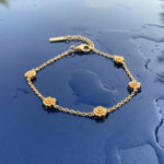 Gold bracelet with five stationary gold rosebud designs spaced out on the chain on a wet blue surface